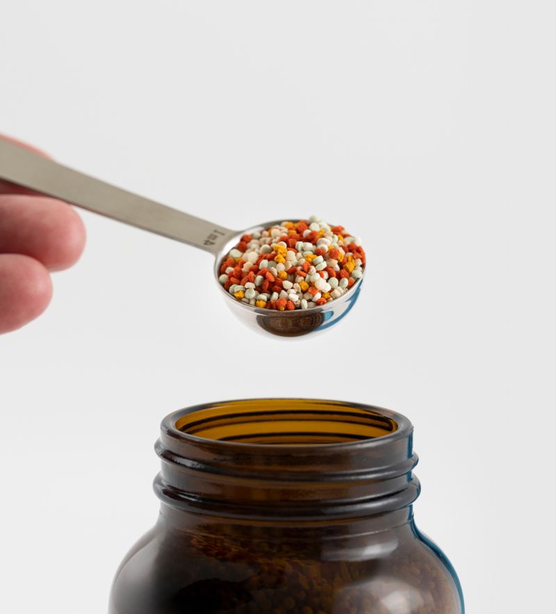 A measuring spoon of Bioniq colored micro-granules above an amber jar